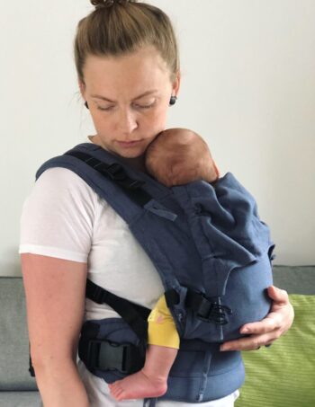 kvinna bär spädbarn i en blå sele av märke Fidella