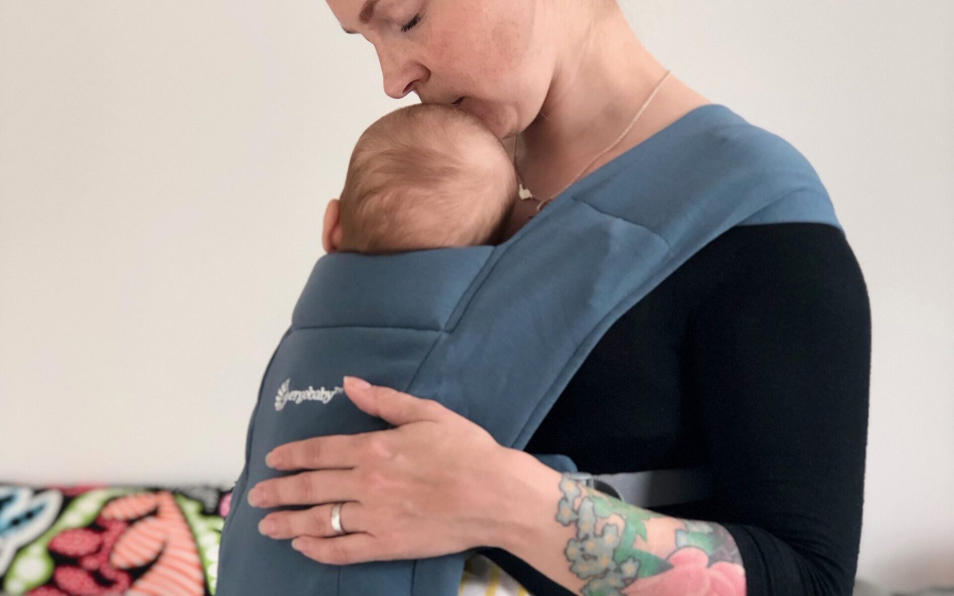 Kvinna bär spädbarn i en blå sele av märke Ergobaby