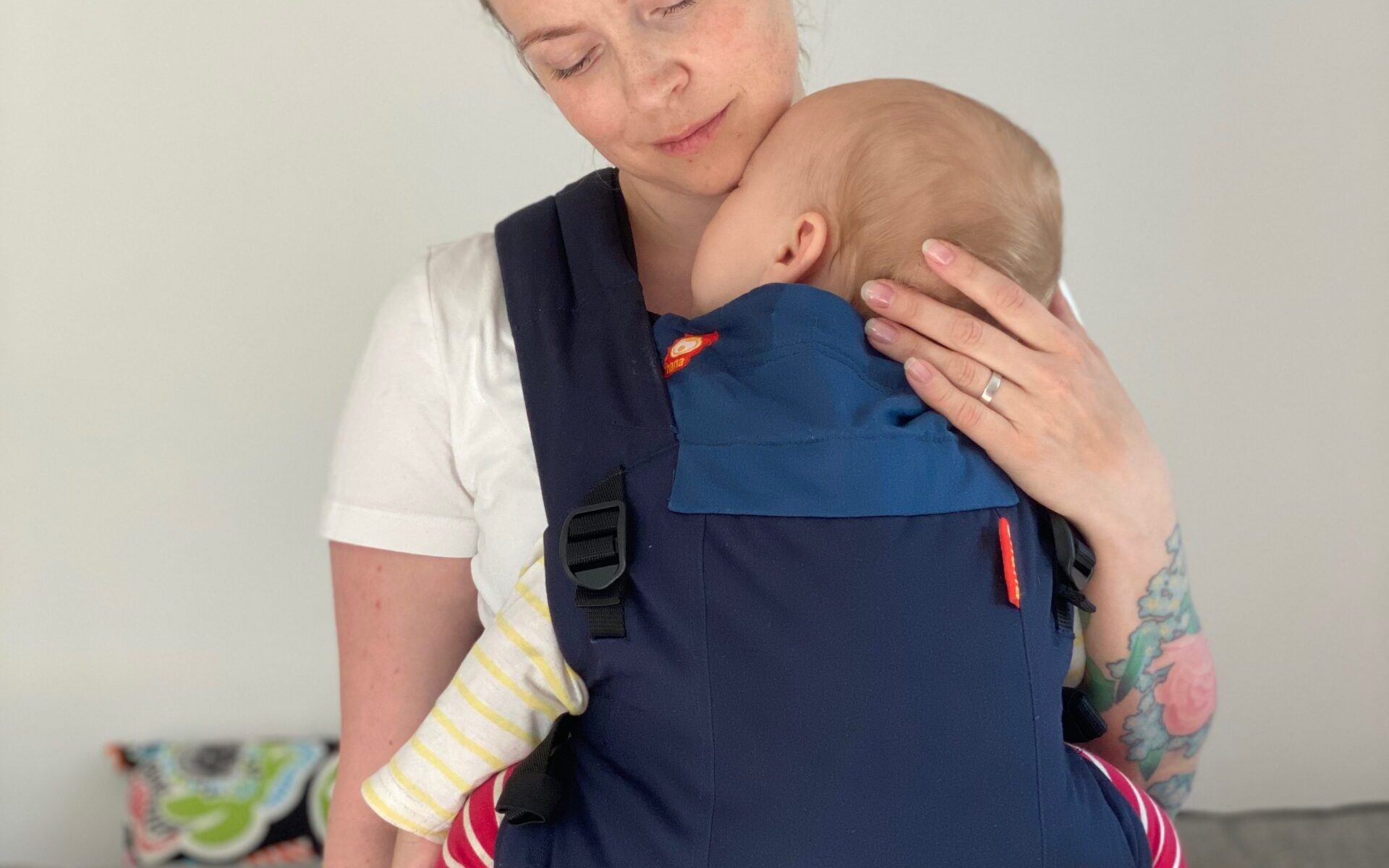 kvinna bär ett barn i en mörkblå bärsele av märke Hana Baby