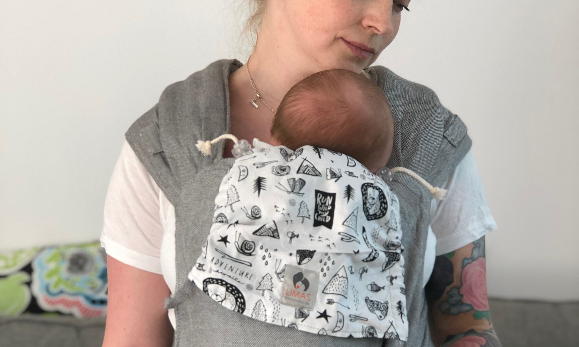 En kvinna bär en liten bebis i en grå halfbuckle från Limas