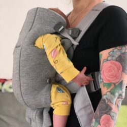 Kvinna bär en liten bebis i en ljusgrå BabyBjörn mini